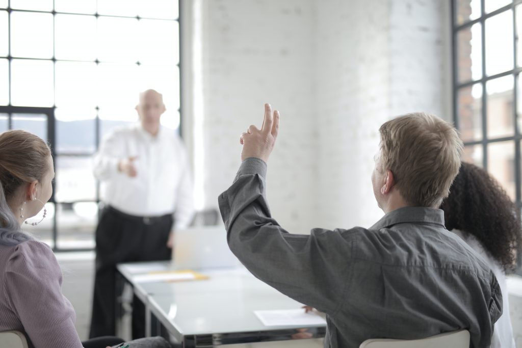 male-employee-raising-hand-for-asking-question-at-conference-3861561